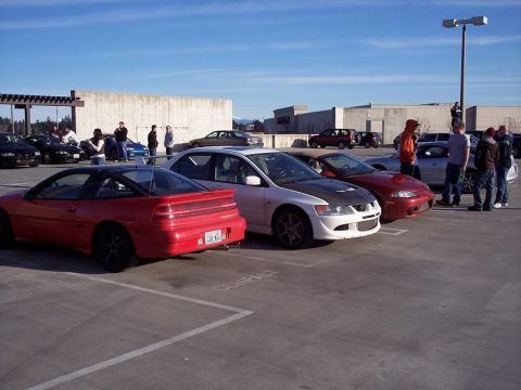 1991 Mitsubishi Eclipse - A red Mitsubishi Eclipse is parked in a lot alongside other vehicles under a clear blue sky.