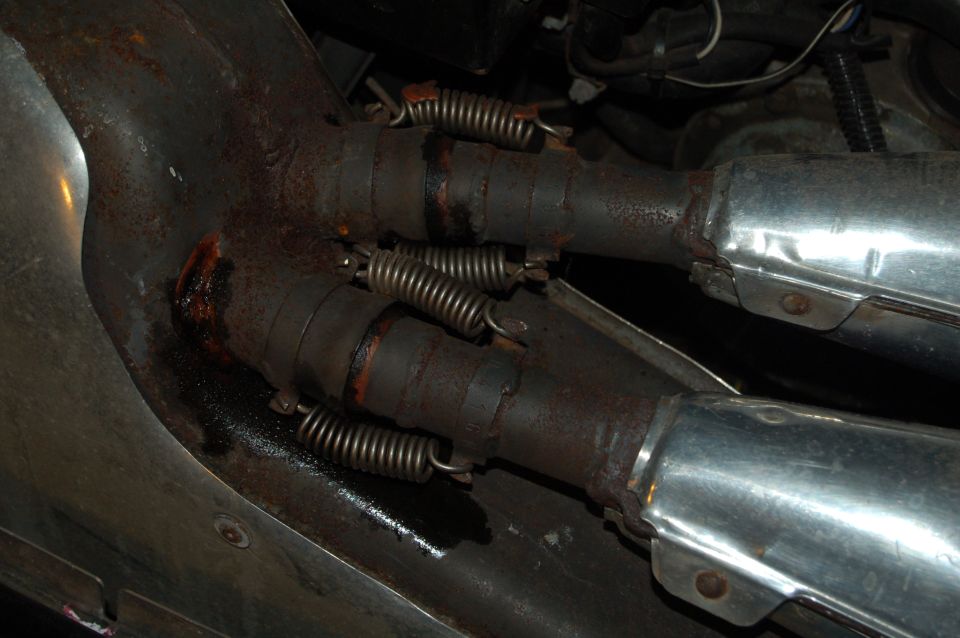 Spring-clipped twin exhaust header joints with rust and sealant residue on a snowmobile