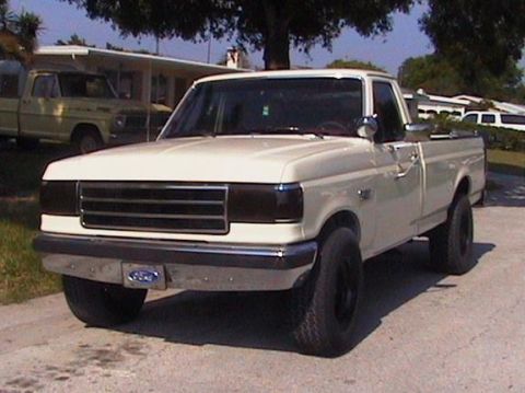 1989 Ford F-250 - A white Ford F-250 pickup truck is parked on a paved surface in front of a house. The truck has blacked-out headlights and a chrome bumper…