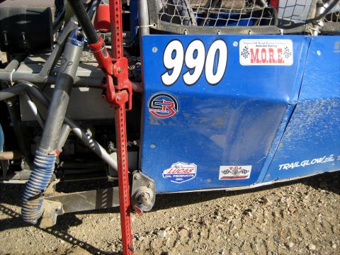 1996 Ford Bronco - A blue off-road race vehicle with the number 990 prominently displayed on its side. A red Hi-Lift jack is mounted vertically next to the ve…