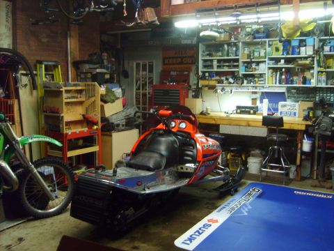 1995 Ford Bronco - An orange and blue Polaris snowmobile is parked in a garage next to a green dirt bike. The garage is filled with tools, shelves, and other…