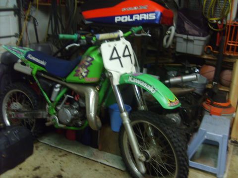 1995 Ford Bronco - A green and blue Kawasaki dirt bike is parked in a cluttered garage. The front number plate has the number 44 on it.