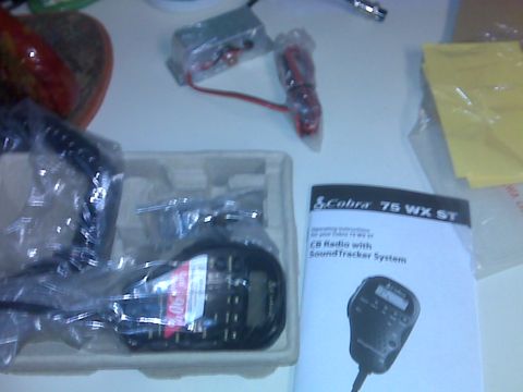 2008 Jeep Wrangler - A Cobra 75 WX ST handheld CB radio unboxed on a white table, still bagged in its foam packing tray alongside the coiled power harness, moun…