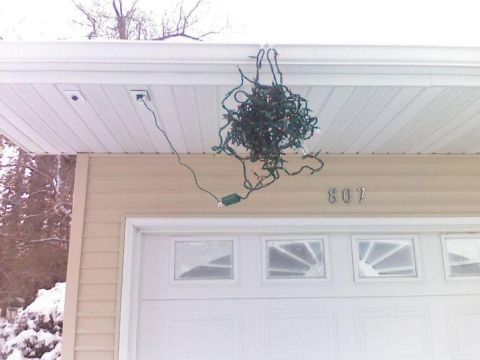 1989 Ford Bronco - A tangled string of Christmas lights hangs from the soffit of a beige house above a white garage door. The house number "807" is visible on…