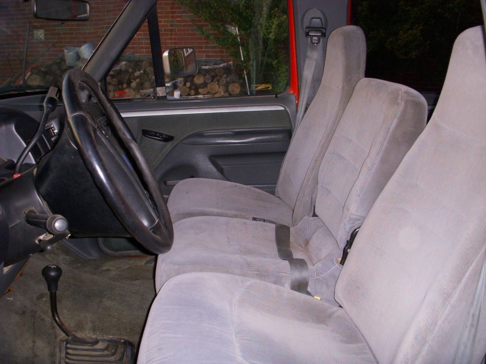 Interior of a pickup truck showing grey fabric seats, steering wheel, and floor shifter.