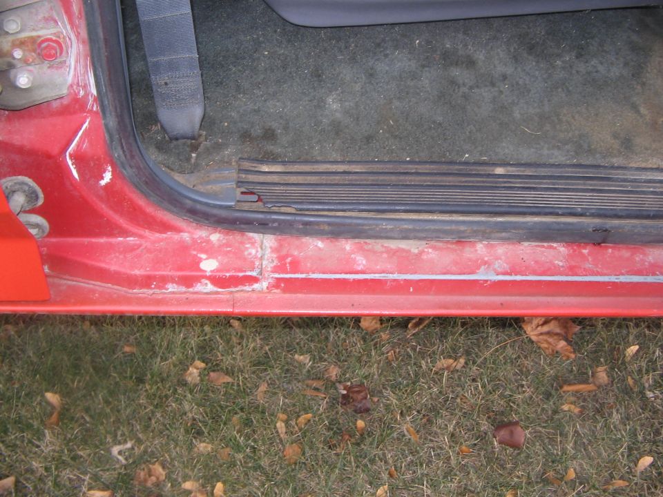 Close-up of red truck door sill and rocker panel with black scuff plate, door open over grass and leaves
