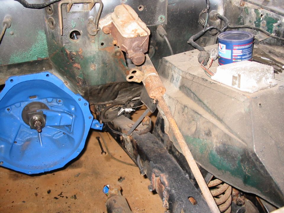 Empty engine bay of green Bronco with blue-painted transmission bellhousing, rusty master cylinder, and Valvoline can