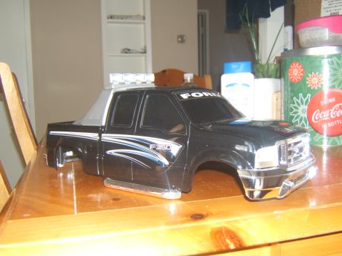 1988 Ford Bronco - A black Ford F-350 pickup truck body is displayed on a wooden table. The body features chrome accents, racing stripes, and a light bar on t…