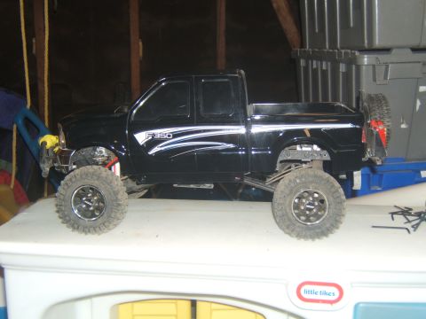 1988 Ford Bronco - A black remote-controlled Ford F-350 pickup truck is shown in profile, resting on a white surface. The truck features large off-road tires…