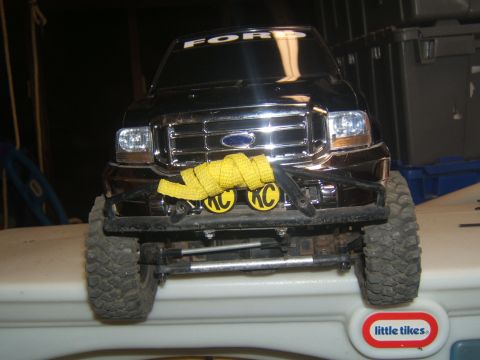 1988 Ford Bronco - The front end of a black Ford F-Series truck is shown, mounted on a white surface. The truck features a chrome grille, headlights, and a ye…