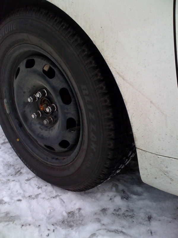 Black tire and steel wheel on a white car in the snow.