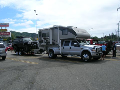 1996 Ford Bronco - A lifted black Ford Bronco is on a trailer towed by a silver Ford F-350 pickup truck with a camper shell. The truck and trailer are parked…