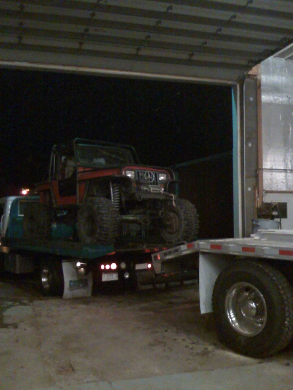 Photo of a Jeep loaded on a rollback flatbed tow truck at night