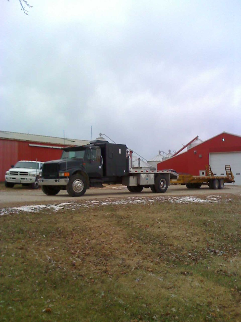 Photo of a black flatbed truck with crew cab towing a trailer in a yard
