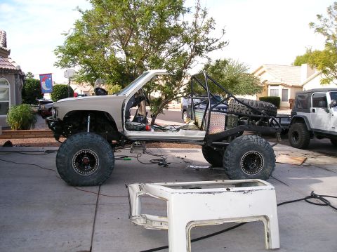 1986 Toyota Hilux - A heavily modified Toyota pickup truck chassis with a roll cage and large off-road tires is parked in a driveway. A white truck bed is plac…