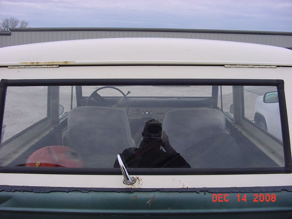Rear window of a white and green 1976 Ford Bronco, reflection of interior and person.