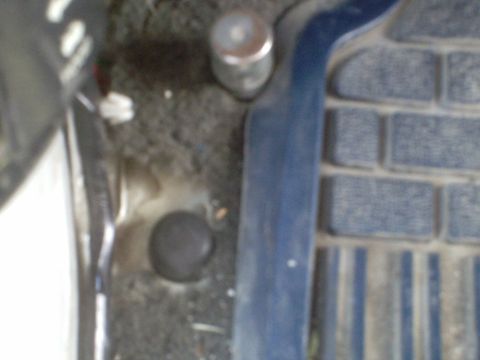 1991 Ford Bronco - A close-up view of the interior floor of a vehicle, showing a black plastic cap and a blue trim piece next to a textured floor mat.