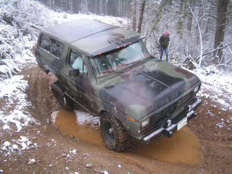 1989 Ford Bronco - A camouflage-painted Ford Bronco is navigating a muddy, snow-dusted off-road trail. The vehicle is angled to the left, with its front tires…