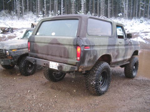 1989 Ford Bronco - The rear driver's side of a camouflage-painted Ford Bronco is shown parked on a dirt and gravel road with a second vehicle partially visibl…