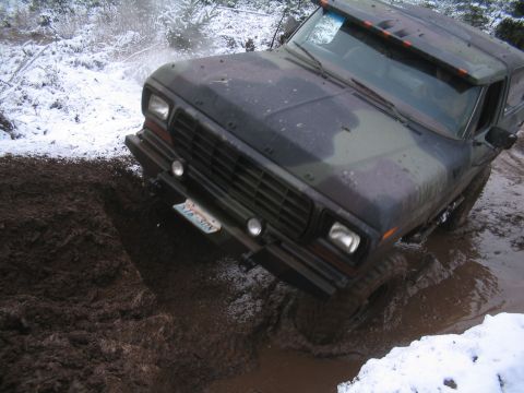 1989 Ford Bronco - A camouflage-painted Ford Bronco is driving through a muddy, snow-covered terrain. The front of the vehicle is angled towards the viewer as…