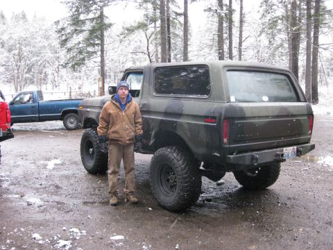 1989 Ford Bronco - A man stands next to a camouflage Ford Bronco with large off-road tires in a snowy, wooded area. A blue pickup truck is visible behind the…