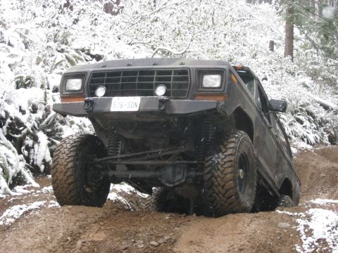 1989 Ford Bronco - A dark colored, lifted Ford Bronco is navigating a muddy, snow-covered trail. The front of the vehicle is angled towards the camera, showin…