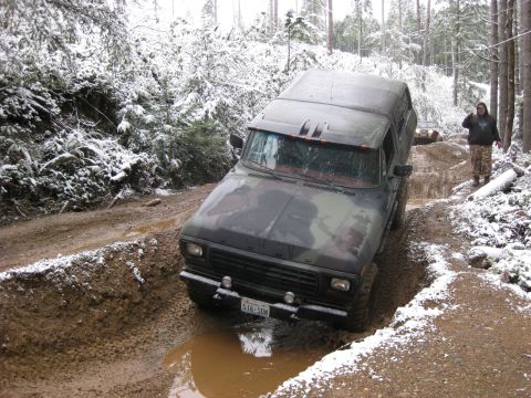 1989 Ford Bronco - A camouflage-painted Ford Bronco is driving through a muddy, snow-covered forest road. Another vehicle is visible in the background, and a…