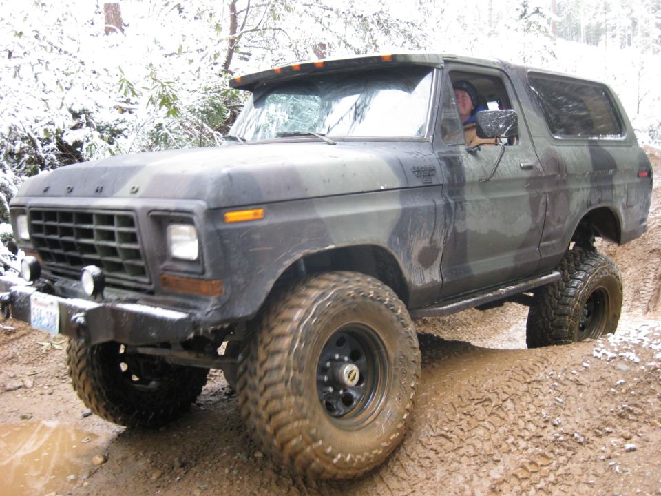 Camouflage Ford Bronco driving through mud and snow off-road.