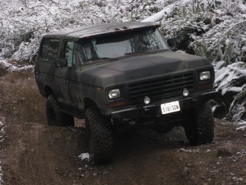 1989 Ford Bronco - A camouflage-painted, lifted Ford Bronco is navigating a muddy, snowy trail. The vehicle is viewed from a 3/4 front angle, showcasing its o…