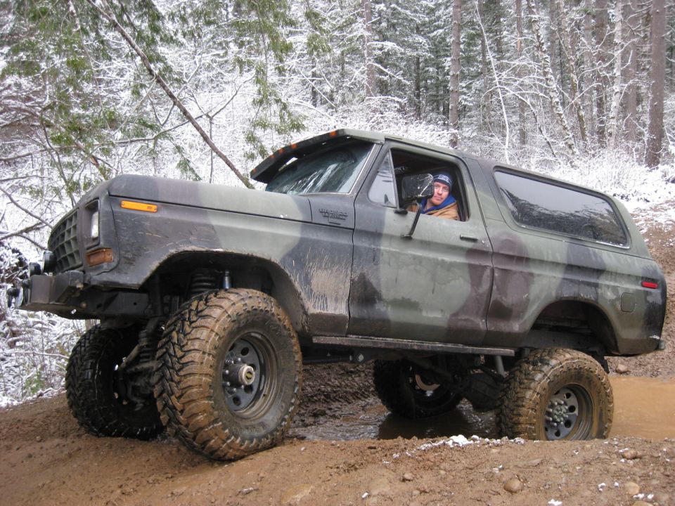 Camouflage Ford Bronco off-roading in a snowy forest.