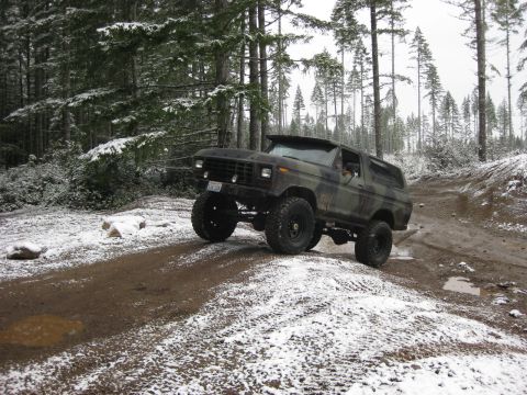 1989 Ford Bronco - A lifted, camouflage-painted Ford Bronco is shown off-road in a snowy forest. The vehicle is angled to the left, with its front right tire…