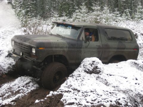 1989 Ford Bronco - A camouflage Ford Bronco is driving through a snowy, muddy forest. The vehicle is partially submerged in mud and snow, with its front tire…