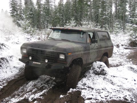 1989 Ford Bronco - A camouflaged Ford Bronco is driving through a muddy, snow-covered forest road. The vehicle appears to be struggling for traction in the ch…