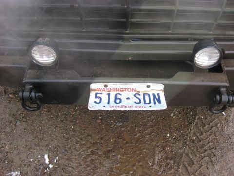 1989 Ford Bronco - The front bumper of a dark green vehicle with a Washington license plate reading "516-SDN" is visible. The vehicle has two round headlights…