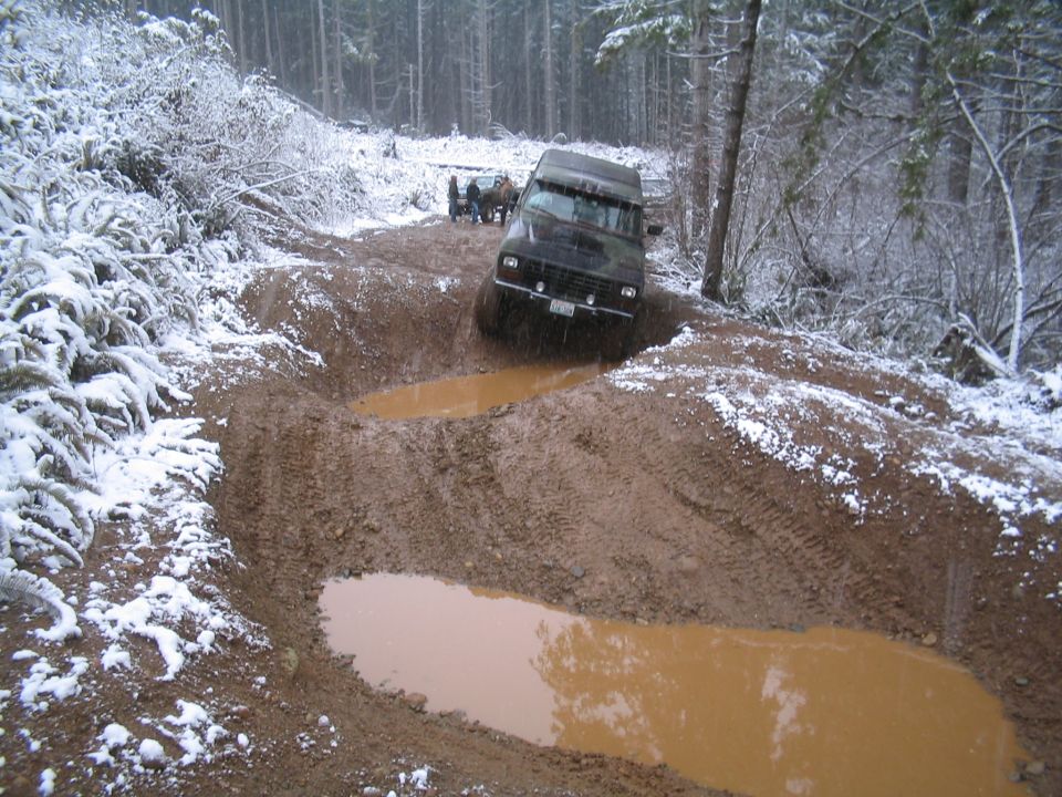 Dark SUV driving through a muddy, snow-covered forest track.