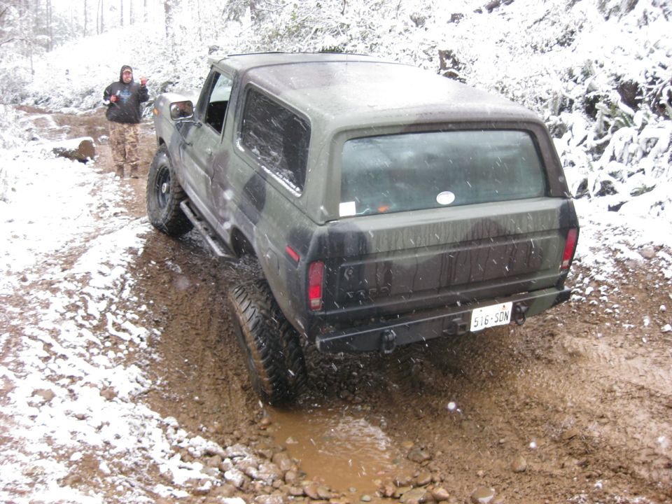 1979 Ford Bronco in camouflage driving through mud and snow.