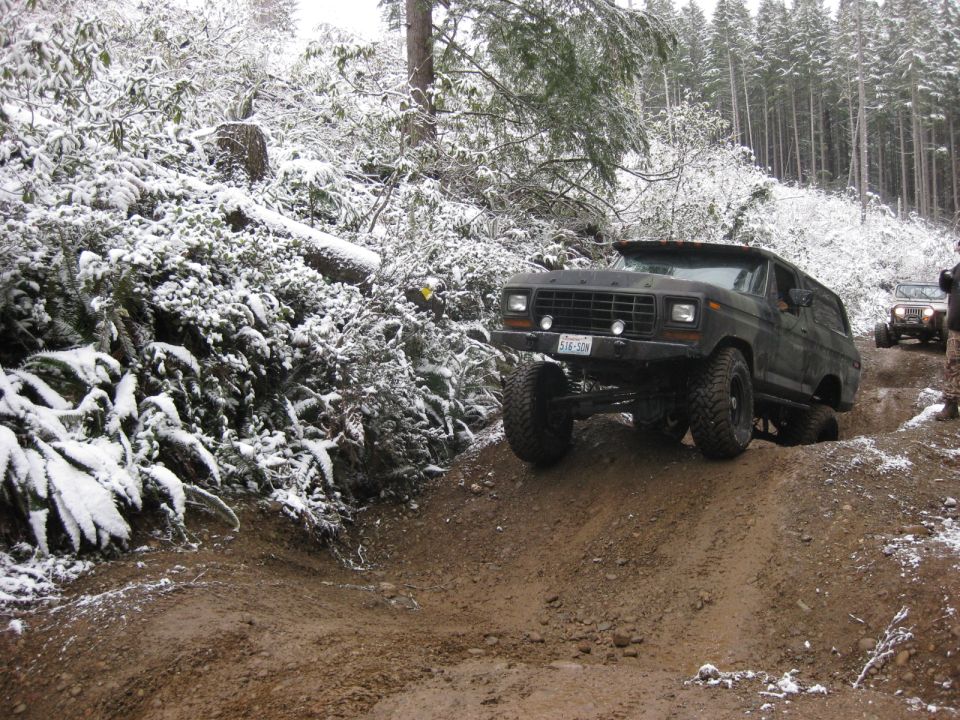 1979 Ford Bronco driving on a muddy, snow-covered trail.