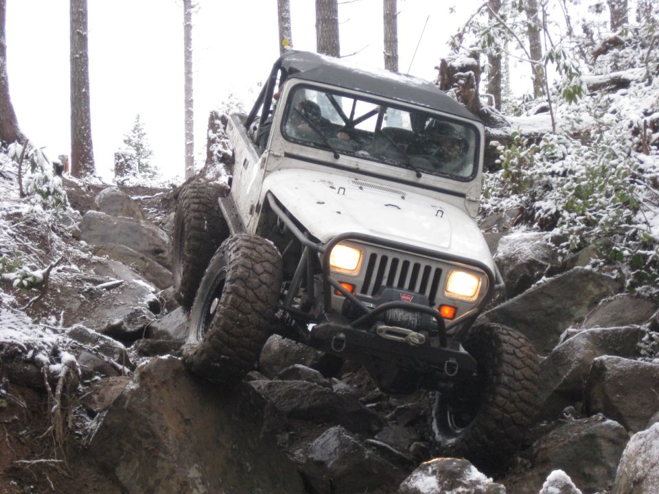 White Jeep Wrangler climbing rocky trail in snow