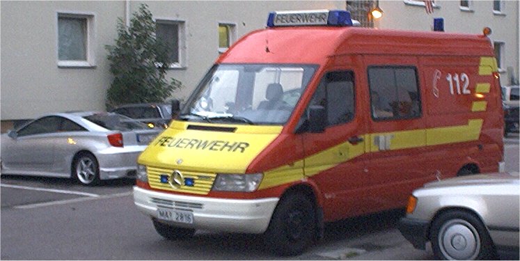 Red and yellow fire department van with 'FEUERWEHR' text, parked next to a silver car