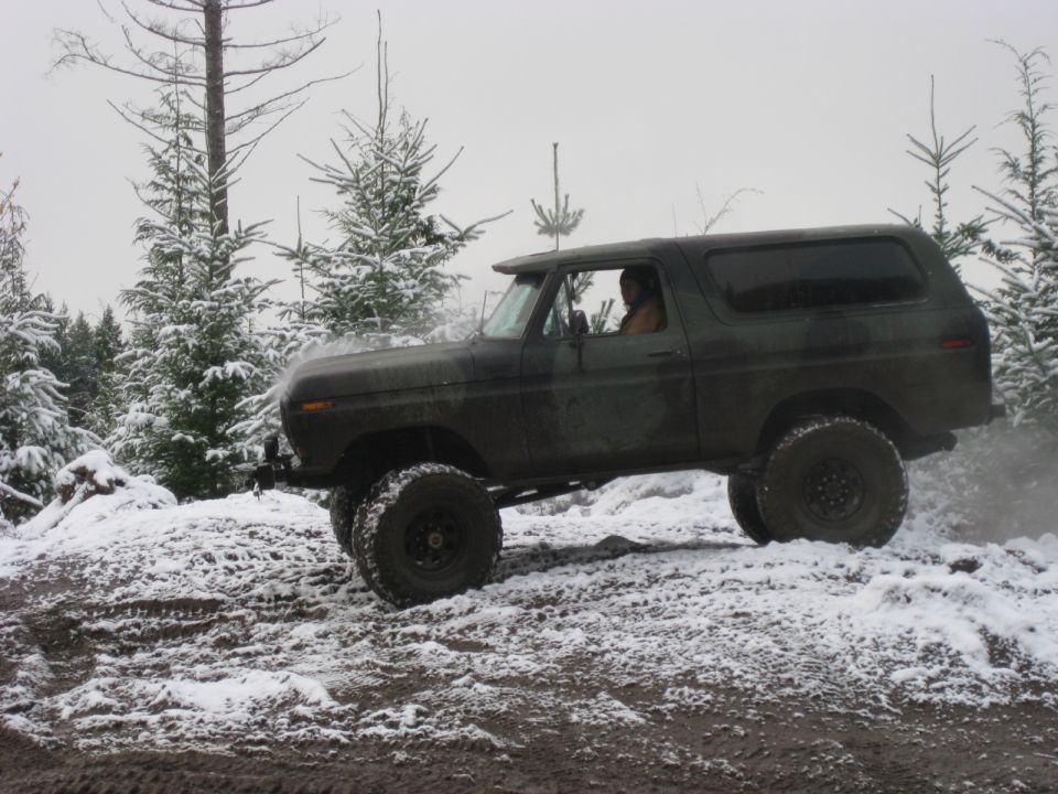 Lifted 1979 Ford Bronco driving off-road in a snowy forest.