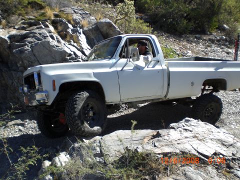 1991 Ford Bronco - A white pickup truck navigates a rocky off-road trail under a clear sky.