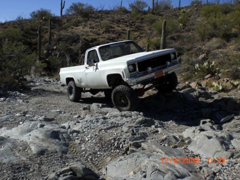 1991 Ford Bronco - This lifted pickup truck navigates a rocky desert terrain under a clear blue sky.