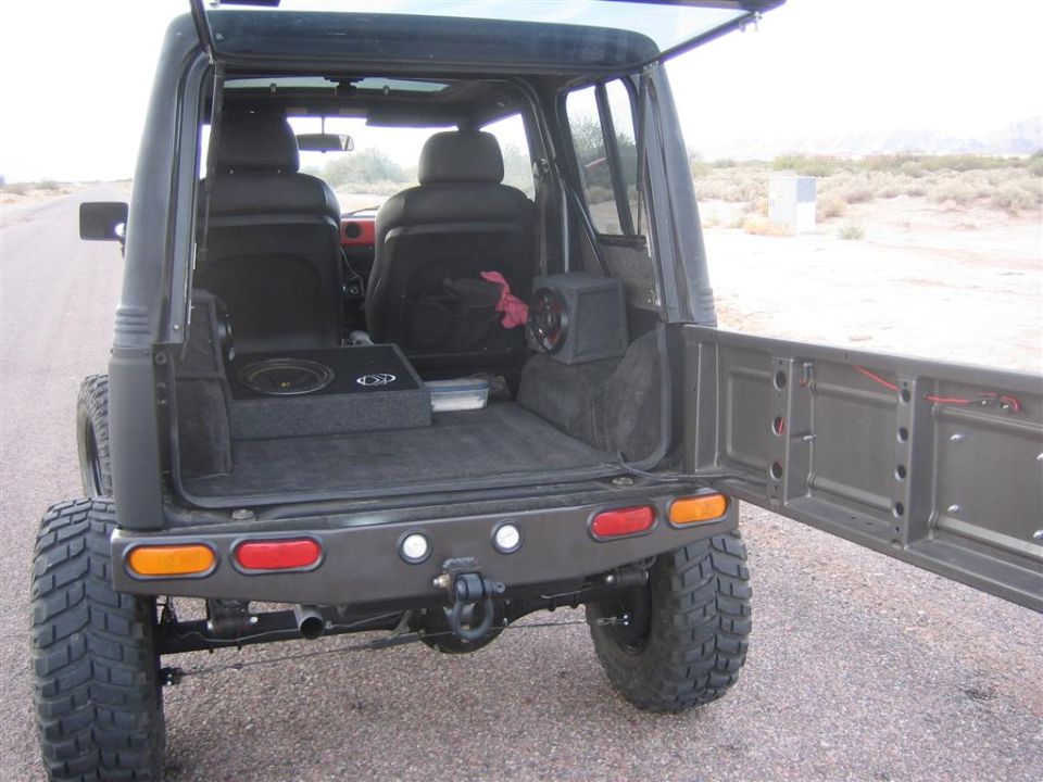 Back view of a lifted 1987 Suzuki Samurai with rear door open, showing custom subwoofers and seats