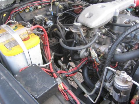 1987 Suzuki Samurai - The engine bay of a vehicle, showing the battery, numerous wires, and engine components.