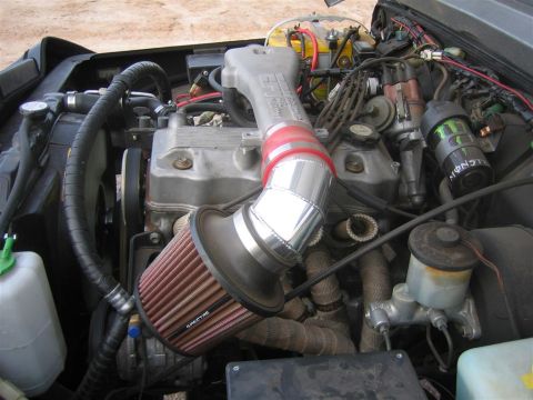 1987 Suzuki Samurai - Engine bay of a 1987 Suzuki Samurai, showing an aftermarket intake and exhaust manifold wrap.