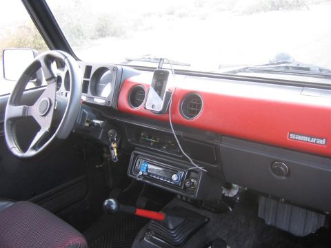 1987 Suzuki Samurai - The dashboard of a Suzuki Samurai features a red accent panel and a mounted iPhone, with a manual transmission visible.