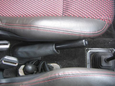 1987 Suzuki Samurai - Close-up of a vehicle's interior, highlighting the seats, handbrake, and gear shifter with red stitching detail.