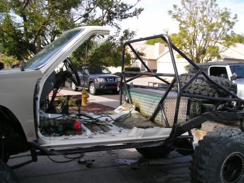 1986 Toyota Hilux - A white custom off-road vehicle is undergoing modifications, with its interior stripped and a roll cage installed.