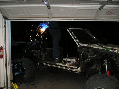 1986 Toyota Hilux - A person welds a custom roll cage onto a heavily modified truck inside a garage.