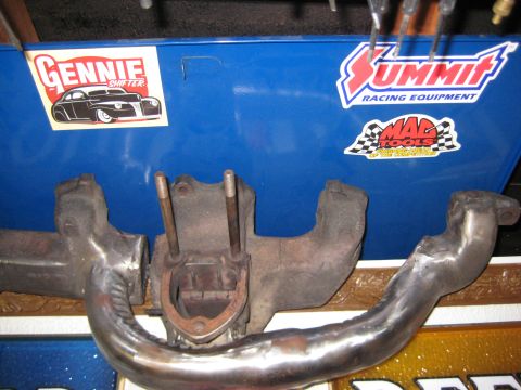 1953 Ford Mainline - Exhaust manifold with various racing equipment stickers visible in the background.